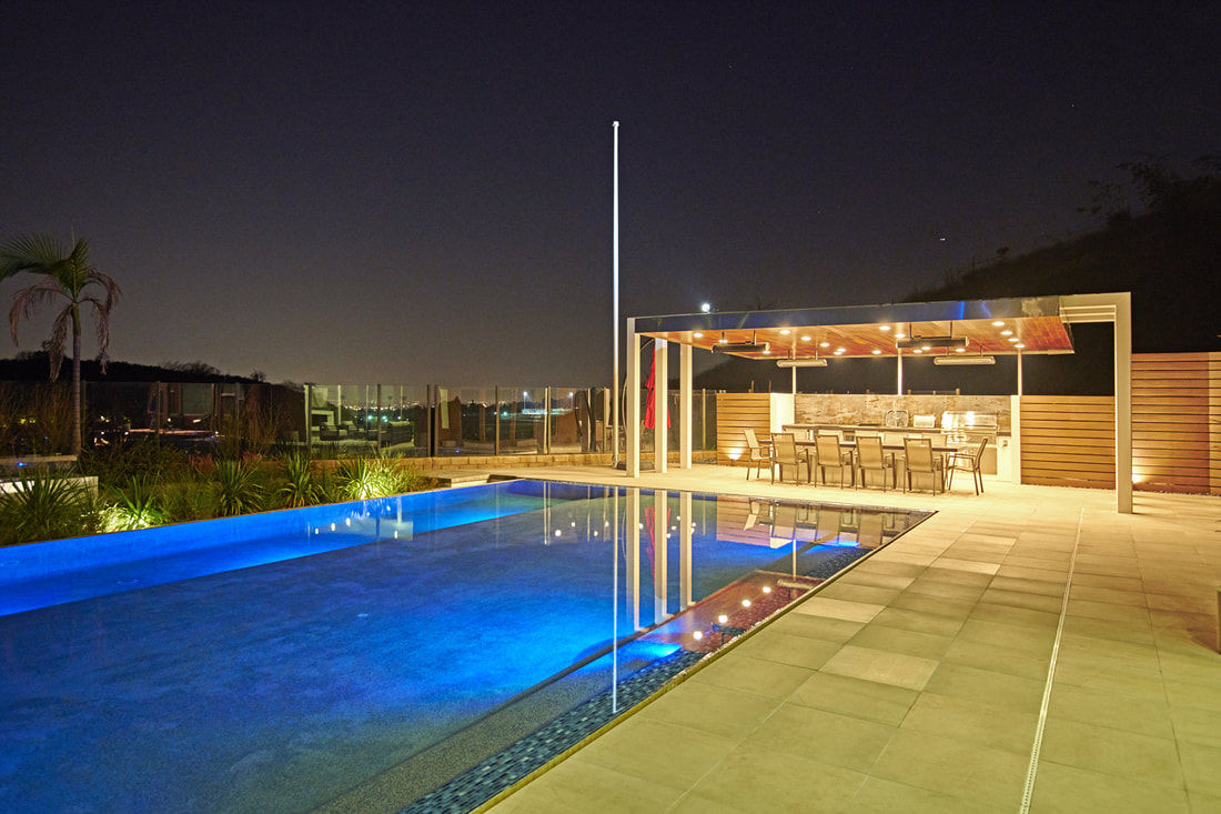Infinity-edge pool and covered outdoor kitchen lit at night, built by Cal Native Construction